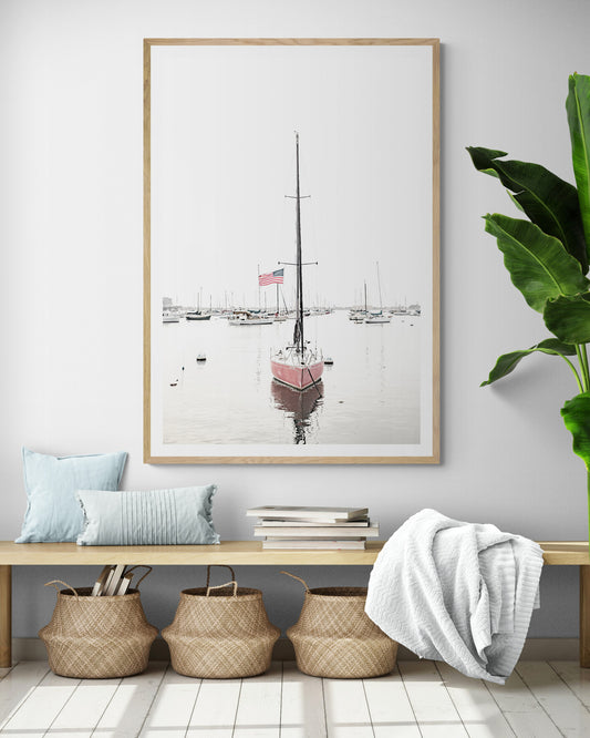A vertical San Diego print featuring a lone red sailboat with an American flag, anchored in a calm San Diego harbor. This minimalist ocean print captures the essence of coastal photography and is perfect for modern coastal decor. Photograph in minimalist mock up.