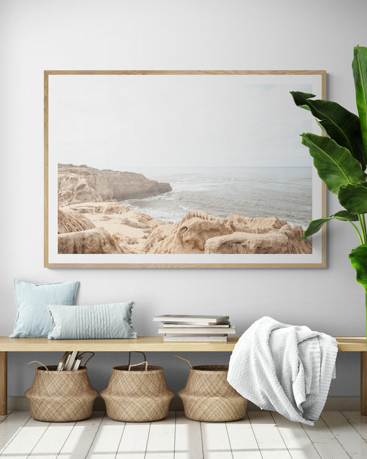 Fine art of Sunset Cliffs, San Diego California horizontal print of hazy high-angle landscape beach photography captures a light blue ocean meeting tall tan and brown cliffs rise as iconic coastal scenery. Photograph in minimalist art mock up.
