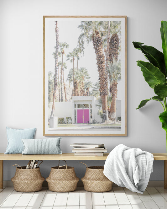 Vertical tropical print featuring a Palm Springs residence with a vibrant pink door, framed by numerous tall palm trees. This image is a fun beach photography style print. Photograph in minimalist mock up.