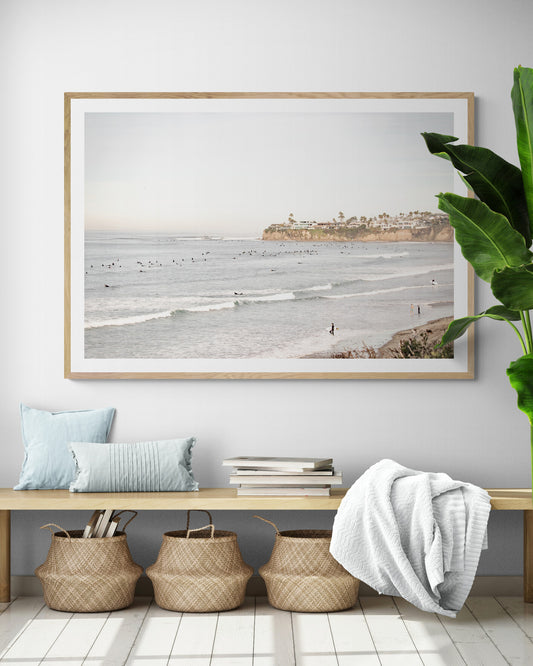 Landscape surf wall decor at Tourmaline Surf Park, Pacific Beach, San Diego, with numerous surfers in the water and a residential cliffside. Photograph in minimalist mock up.