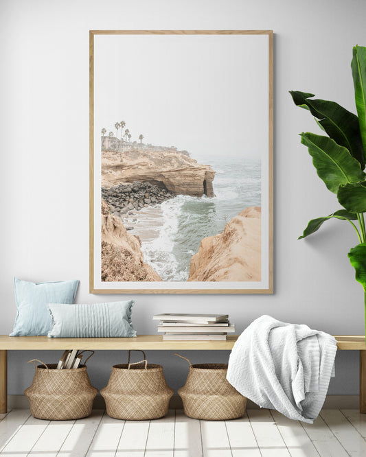 Fine art of Sunset Cliffs, San Diego California vertical print of hazy high-angle landscape beach photography captures a light blue ocean meeting tall tan, rocky, brown cliffs rise as iconic coastal scenery. Photograph in minimalist mock up.