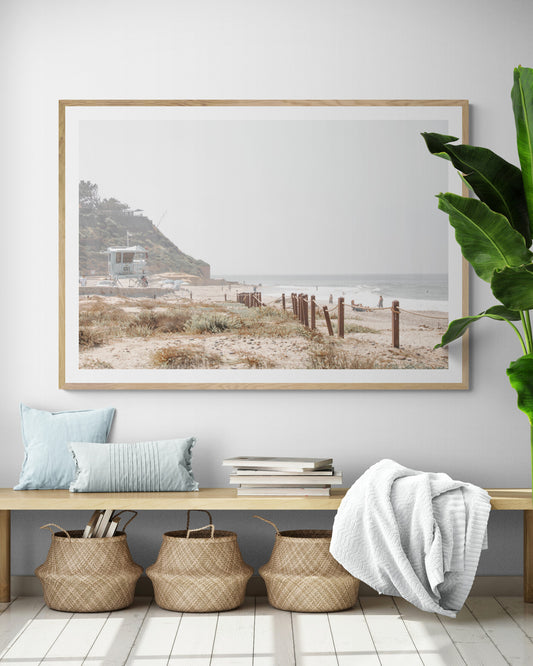 Landscape coastal photography of a light-colored lifeguard tower at a Southern California beach, with a rustic wooden fence leading towards the ocean waves. This tranquil beachscape print is ideal for beach cottage wall decor or a calm beach print. Photograph in minimalist mock up.