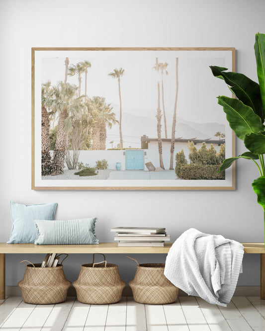 Coastal print of a Palm Springs home with a bright blue door, surrounded by tall palm trees and distant mountains, embodying summer vibes wall art. Photograph in minimalist mock up.