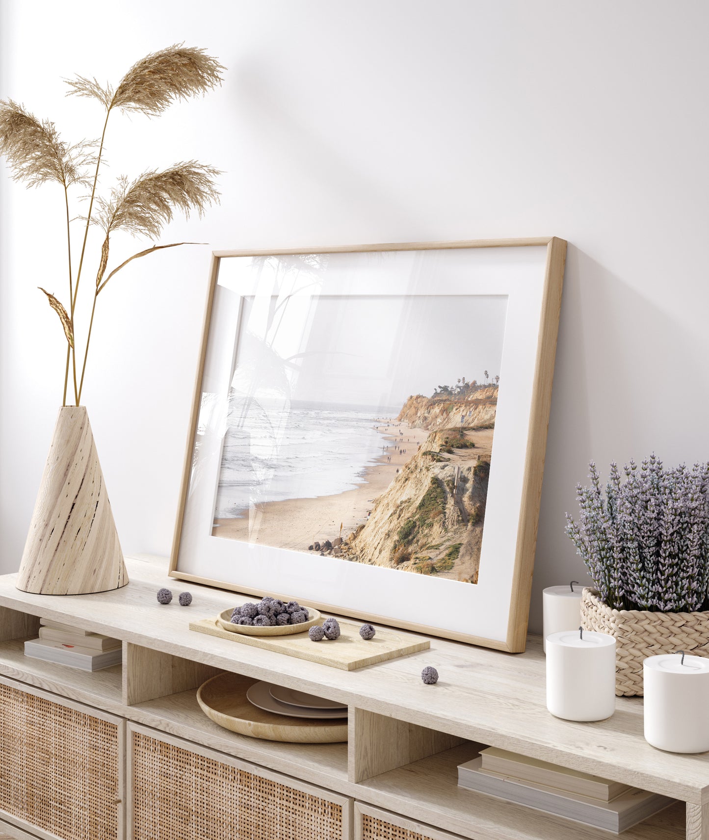 Fine art of Torrey Pines, San Diego California horizontal print of hazy high-angle landscape beach photography captures a light blue ocean meeting a sandy beach with many beach goers. To the right, tall tan and brown cliffs rise as iconic coastal scenery. Photograph in minimalist framed mock up.