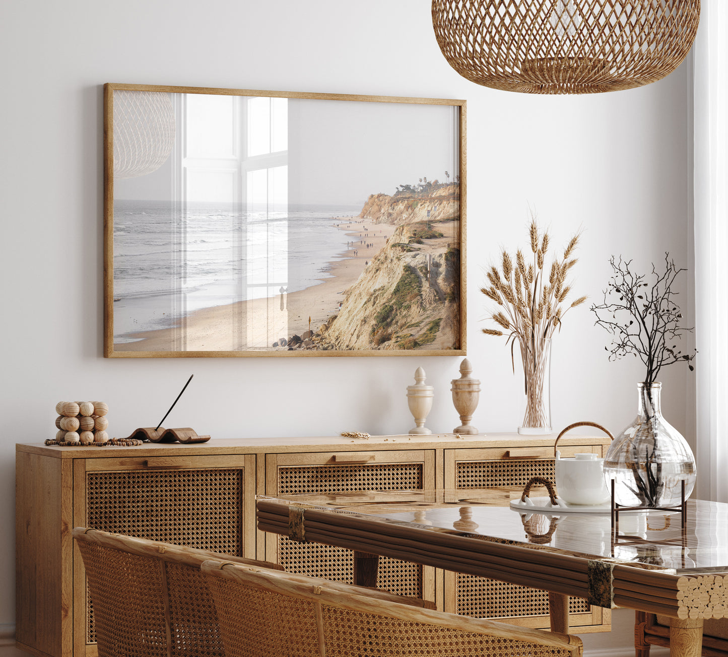 Fine art of Torrey Pines, San Diego California horizontal print of hazy high-angle landscape beach photography captures a light blue ocean meeting a sandy beach with many beach goers. To the right, tall tan and brown cliffs rise as iconic coastal scenery. Photograph in minimalist framed dining room mock up.