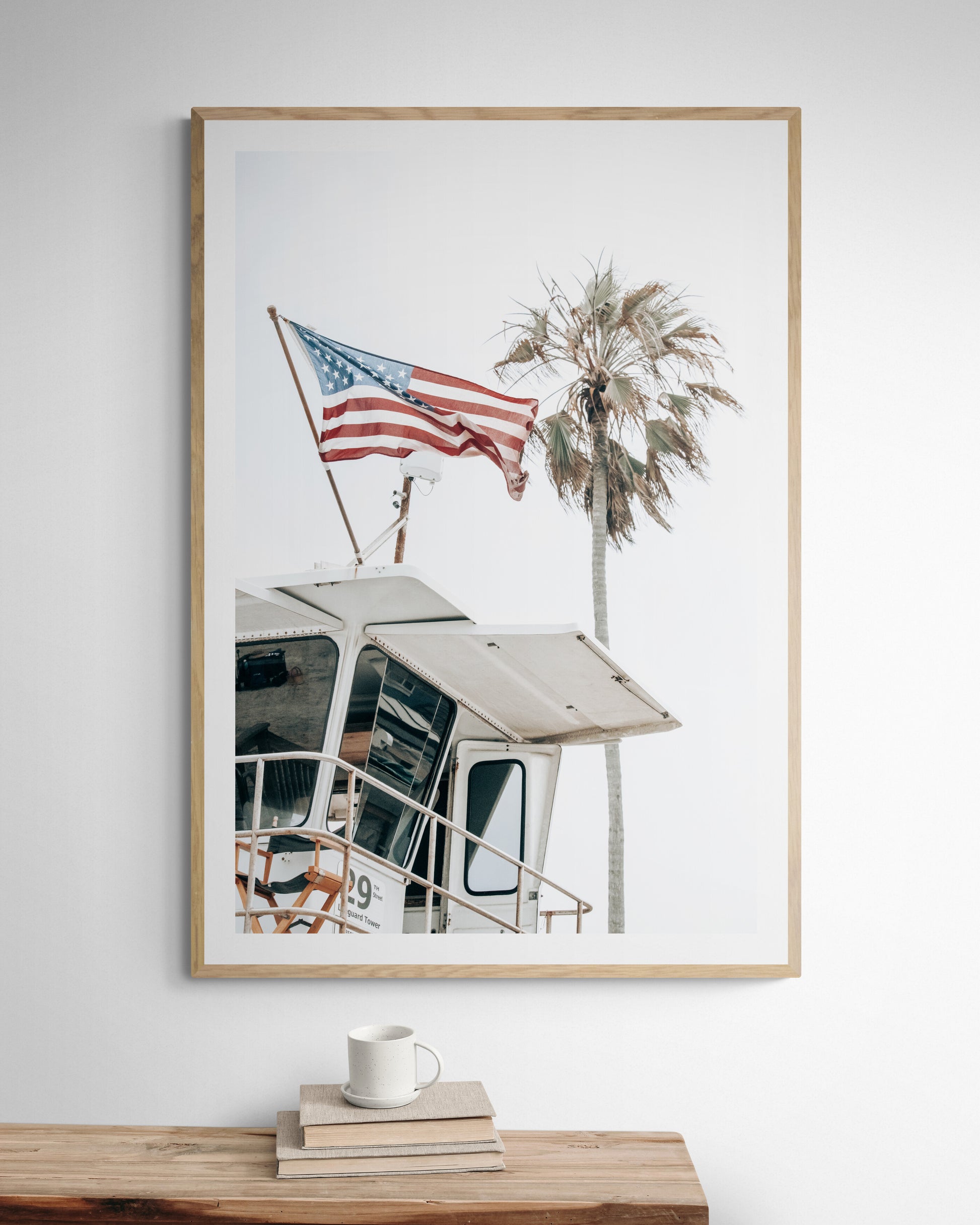 An American flag attached to a lifeguard tower with palm trees in the background, captured in California with a clear sky in the top half of the image. Photograph in minimalist mock up.