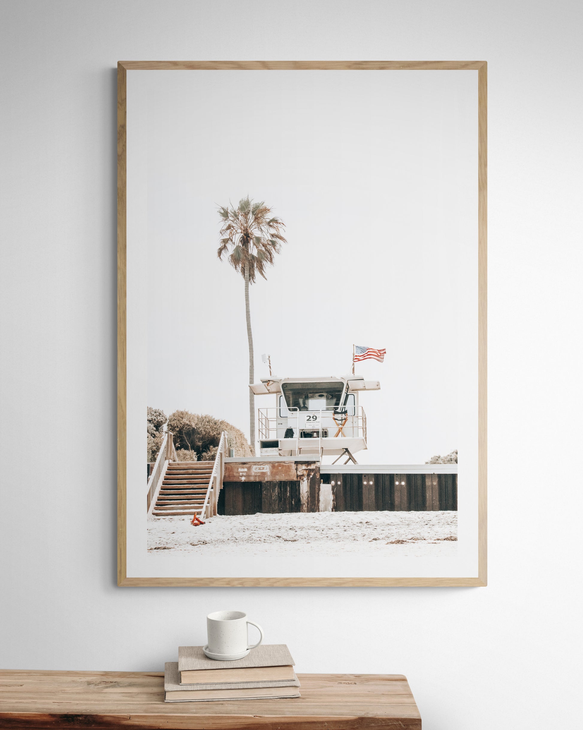 A photograph featuring an American flag on a lifeguard tower with a palm tree in the background, taken at a beach in Del Mar, San Diego. Photograph in minimalist mock up.
