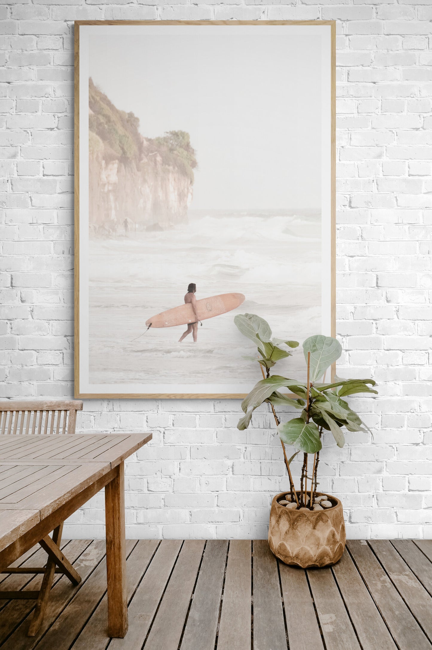 Vertical surf art print of a lone surfer carrying a surfboard, walking on a rocky, foggy shoreline at Moonlight State Beach with a lifeguard tower and cliff in the background. Photograph in minimalist mock up.