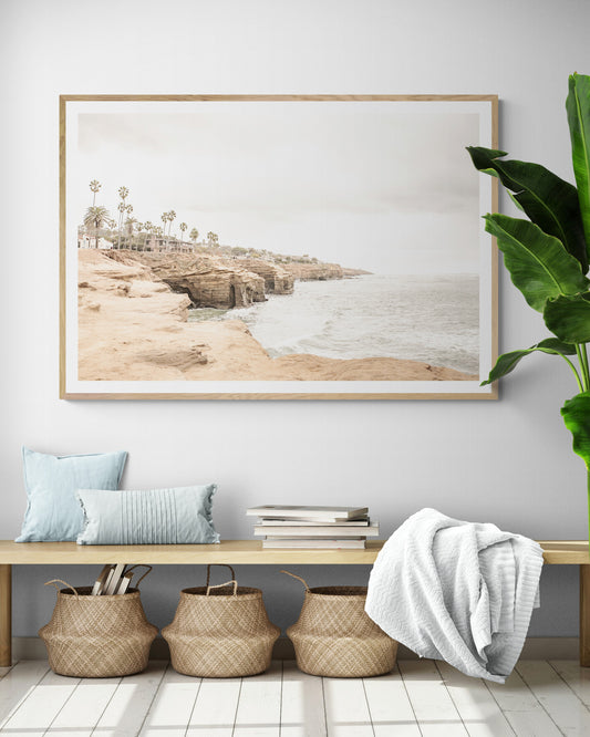 Fine art of Sunset Cliffs, San Diego California horizontal print of hazy high-angle landscape beach photography captures a light blue ocean meeting tall tan, brown cliffs rise as iconic coastal scenery. Photograph in minimalist mock up.