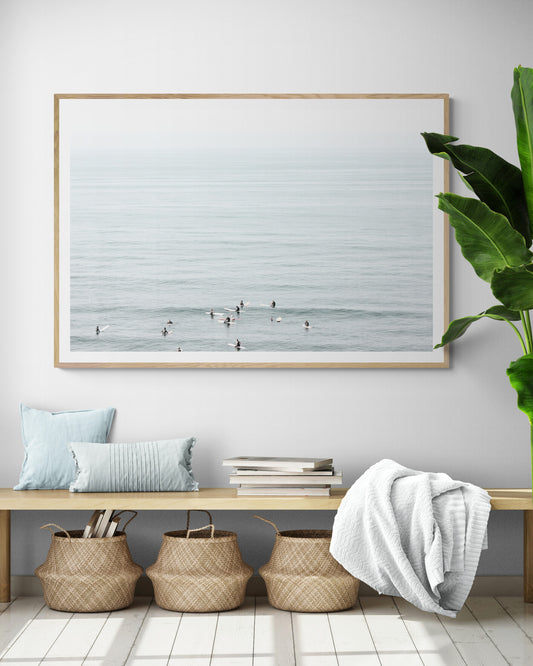 Horizontal surf art showing multiple surfers waiting in the calm ocean water for waves, with a hazy Southern California coastline in the distance. This minimalist surf print captures authentic surf vibes. Photograph in minimalist mock up.