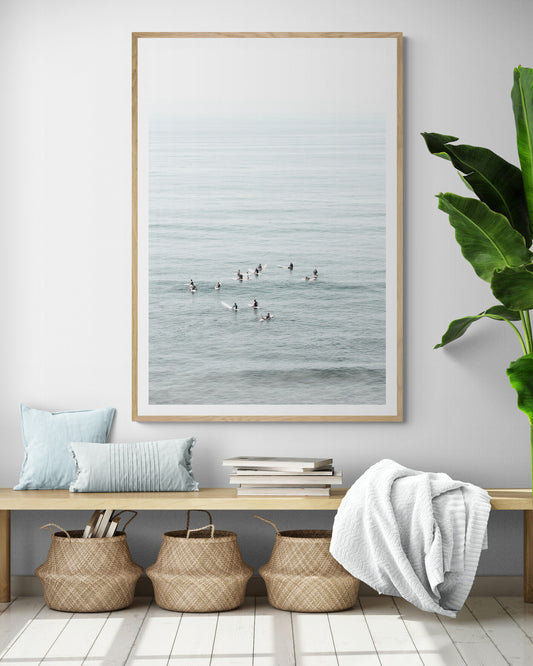 Vertical surf art showing multiple surfers waiting in the calm ocean water for waves, with a hazy Southern California coastline in the distance. This minimalist surf print captures authentic surf vibes. Photograph in minimalist mock up.