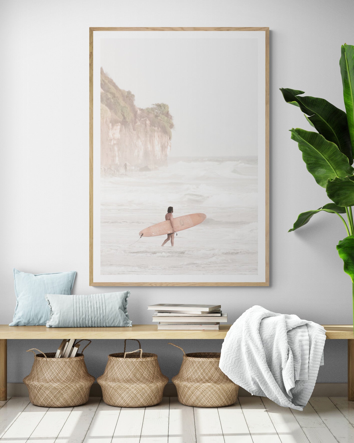 Vertical surf art print of a lone surfer carrying a surfboard, walking on a rocky, foggy shoreline at Moonlight State Beach with a lifeguard tower and cliff in the background. Photograph in minimalist mock up.