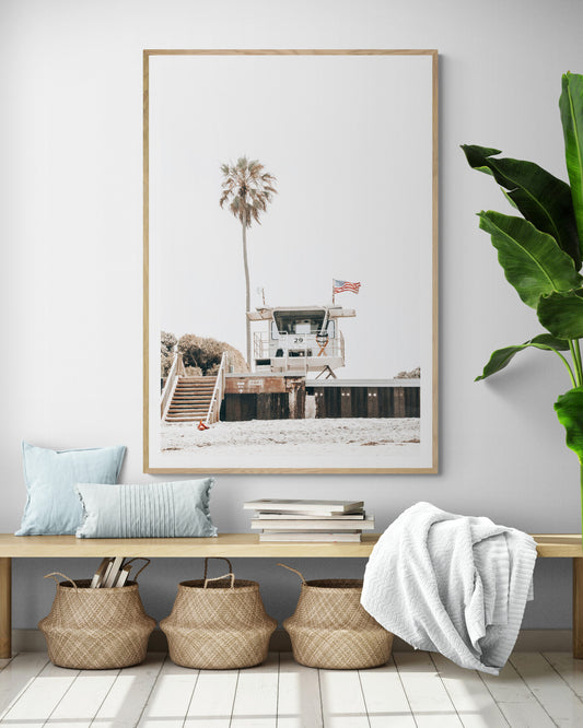 A photograph featuring an American flag on a lifeguard tower with a palm tree in the background, taken at a beach in Del Mar, San Diego. Photograph in minimalist mock up.