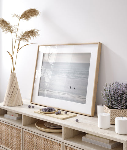 Horizontal minimalist ocean art with a close-up blue waves print of water, featuring subtle ripples and soft textures, ideal as a neutral ocean print, two surfers sit and watch the waves. Photograph in minimalist mock up.