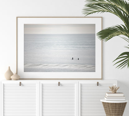 Horizontal minimalist ocean art with a close-up blue waves print of water, featuring subtle ripples and soft textures, ideal as a neutral ocean print, two surfers sit and watch the waves. Photograph in minimalist mock up.