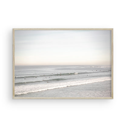 A wide landscape surf wall decor shot of Pacific Beach, showing many surfers in the water catching gentle waves under a hazy sky. This neutral surf print is great for beach art. Photograph in minimalist mock up.