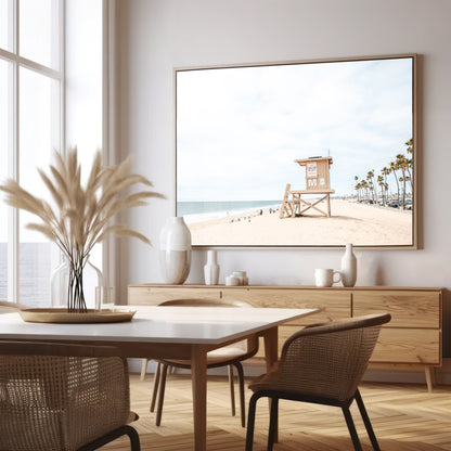 A wide landscape coastal photography view of Newport Beach in Southern California, featuring a row of tall palm trees, a lifeguard tower, and people enjoying the calm beach. Photograph in minimalist mock up.