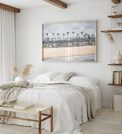 Landscape beach photography of Newport Beach, California, showing a wide sandy beach, a long line of tall palm trees, and coastal homes. Photograph in minimalist mock up.