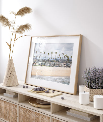 Landscape beach photography of Newport Beach, California, showing a wide sandy beach, a long line of tall palm trees, and coastal homes. Photograph in minimalist mock up.