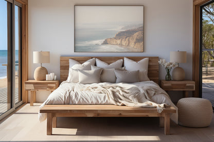 Fine art of Torrey Pines, San Diego California horizontal print of hazy high-angle landscape beach photography captures a light blue ocean meeting a sandy beach with many beach goers. To the right, tall tan and brown cliffs rise as iconic coastal scenery. Photograph in minimalist framed bedroom mock up.