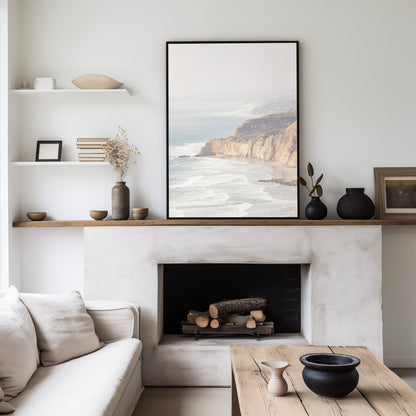 Fine art of Torrey Pines, San Diego California vertical print of hazy high-angle landscape beach photography captures a light blue ocean meeting a sandy beach with many beach goers. To the right, tall tan and brown cliffs rise as iconic coastal scenery. Photograph in minimalist framed mock up.