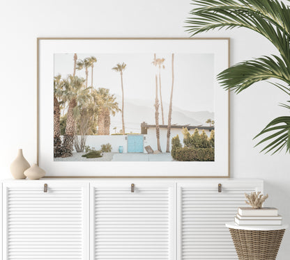 Coastal print of a Palm Springs home with a bright blue door, surrounded by tall palm trees and distant mountains, embodying summer vibes wall art. Photograph in minimalist mock up.