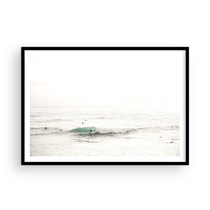 Fine art of horizontal landscape print by Southern California photographer Kim Dybczak of Salt Creek Prints, featuring a bright image captures a pale sandy beach giving way to a vast, light gray ocean with gentle waves. Several surfers are scattered across the water, some sitting on their boards and others riding small waves. The sky is a uniform, pale white, creating a soft, overcast atmosphere, located in Windansea Beach in La Jolla, California. Photograph in framed minimalist mock up