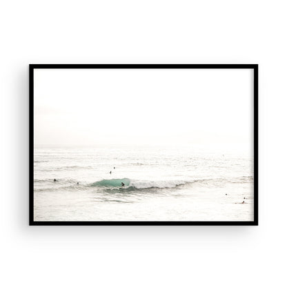 Fine art of horizontal landscape print by Southern California photographer Kim Dybczak of Salt Creek Prints, featuring a bright image captures a pale sandy beach giving way to a vast, light gray ocean with gentle waves. Several surfers are scattered across the water, some sitting on their boards and others riding small waves. The sky is a uniform, pale white, creating a soft, overcast atmosphere, located in Windansea Beach in La Jolla, California. Photograph in framed minimalist mock up