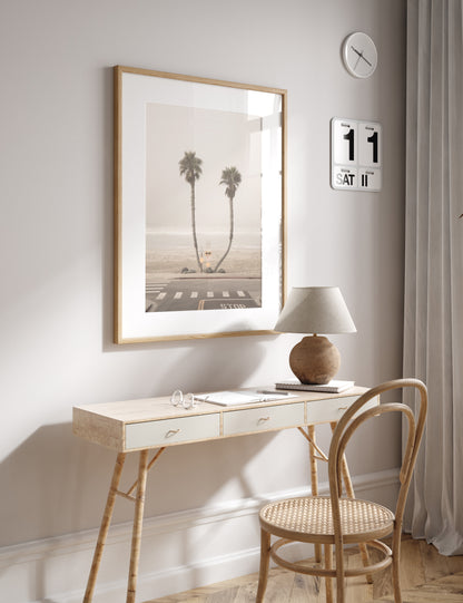 Vertical coastal photography of two leaning palm trees on a hazy Oceanside beach, with ocean waves in the background and a crosswalk in the foreground. Photograph in minimalist mock up.