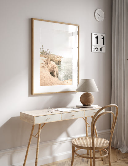 Fine art of Sunset Cliffs, San Diego California vertical print of hazy high-angle landscape beach photography captures a light blue ocean meeting tall tan, brown cliffs rise as iconic coastal scenery. Photograph in minimalist mock up.