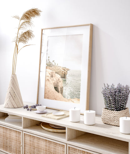 Fine art of Sunset Cliffs, San Diego California vertical print of hazy high-angle landscape beach photography captures a light blue ocean meeting tall tan, brown cliffs rise as iconic coastal scenery. Photograph in minimalist mock up.