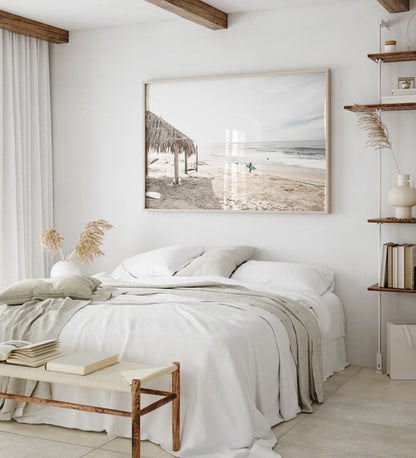 Fine art of WindanSea Beach, La Jolla California horizontal landscape print by Southern California photographer Kim Dybczak of Salt Creek Prints, featuring a bright, slightly desaturated image shows Windansea Beach in La Jolla, California. A thatched beach hut stands on the sandy shore in the left foreground. Further down the beach, a surfer carrying a teal surfboard walks towards the ocean where several other surfers are visible in the water. Photograph in minimalist framed bedroom mock up