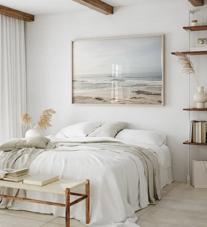 Fine art of horizontal landscape print by Southern California photographer Kim Dybczak of Salt Creek Prints, featuring a bright image captures a pale sandy beach giving way to a vast, light gray ocean with gentle waves. Several surfers are scattered across the water, some sitting on their boards and others riding small waves. The sky is a uniform, pale white, creating a soft, overcast atmosphere, located in Windansea Beach in La Jolla, California. Photograph in framed minimalist mock up