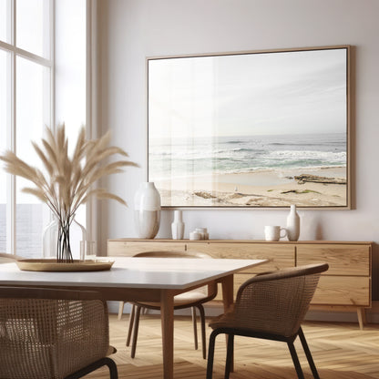 Fine art of horizontal landscape print by Southern California photographer Kim Dybczak of Salt Creek Prints, featuring a bright image captures a pale sandy beach giving way to a vast, light gray ocean with gentle waves. Several surfers are scattered across the water, some sitting on their boards and others riding small waves. The sky is a uniform, pale white, creating a soft, overcast atmosphere, located in Windansea Beach in La Jolla, California. Photograph in framed dining minimalist mock up