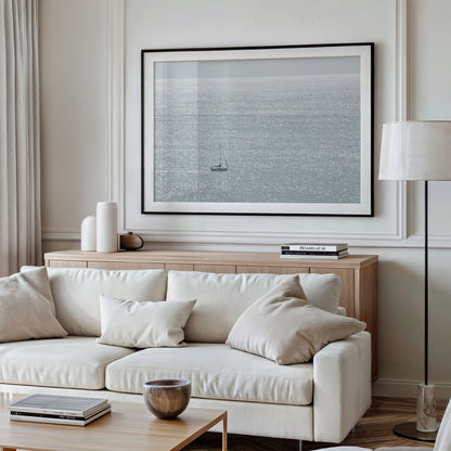 Large minimalist ocean print showing a smooth seascape with gentle ocean waves meeting a clear horizon line, one single sail boat in the distance. This calm nautical print provides a serene view in Dana Point, San Diego, California. Photograph in minimalist mock up.