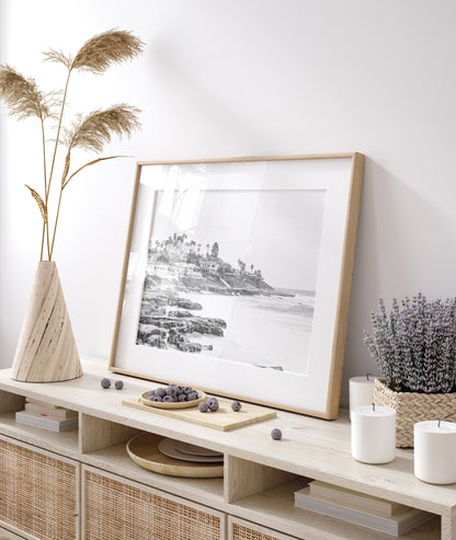 Fine art of WindanSea Beach, La Jolla California horizontal landscape black and white print by Southern California photographer Kim Dybczak of Salt Creek Prints, featuring a powerful waves crashing against the rocky shore of California coast. Beach homes and palm trees sit atop the cliffside, with stairs leading down to a sheltered area. Photograph in minimalist framed mock up