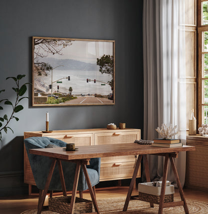A hazy eye-level shot of San Diego Streets looks down a sloping road featuring red traffic lights and "Carmel Valley" signs, capturing a Local Surf Print vibe. The foreground of this California Wall Art showcases landscape and cars, framed by tree branches at the top, adding to the San Diego Photo aesthetic. The lighting suggests a hazy daytime, perfect for Minimalist Beach Wall Art. This horizontal San Diego print makes a great piece of horizontal beach wall decor. Photograph in minimalist office mock up