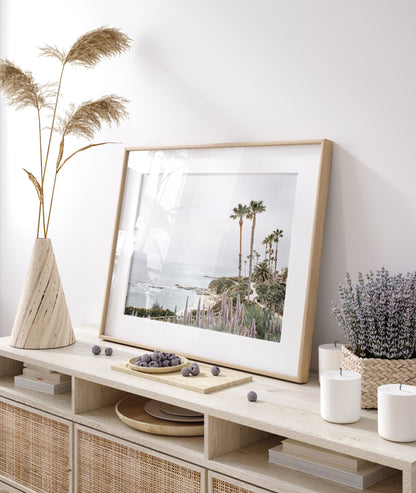 Horizontal coastal photography featuring a scenic view of the ocean with palm trees in the background, set against a white sky, located in Laguna California. Photograph in minimalist mock up.