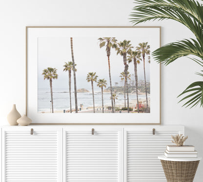 Horizontal coastal photography of a beachscape at Laguna Beach, California, beach art print featuring palm trees and a clear blue sky with a few clouds over a beach scene. Photograph in minimalist mock up.