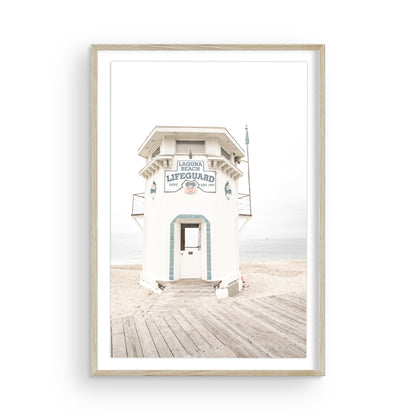 Vertical coastal photography of a white lifeguard tower at Laguna Beach, California, with a clear blue sky and ocean in the background. This neutral ocean print highlights coastal architecture. Photograph in minimalist mock up.