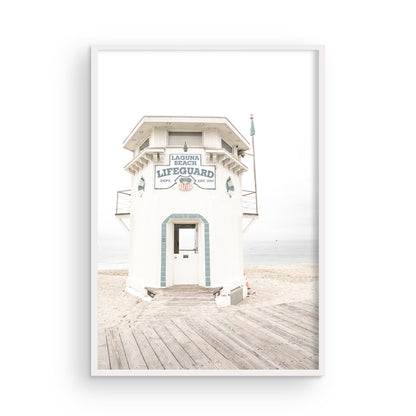 Vertical coastal photography of a white lifeguard tower at Laguna Beach, California, with a clear blue sky and ocean in the background. This neutral ocean print highlights coastal architecture. Photograph in minimalist mock up.