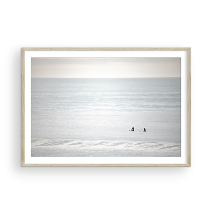 Horizontal minimalist ocean art with a close-up blue waves print of water, featuring subtle ripples and soft textures, ideal as a neutral ocean print, two surfers sit and watch the waves. Photograph in minimalist mock up.