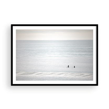 Horizontal minimalist ocean art with a close-up blue waves print of water, featuring subtle ripples and soft textures, ideal as a neutral ocean print, two surfers sit and watch the waves. Photograph in minimalist mock up.