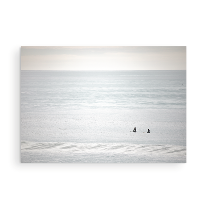 Horizontal minimalist ocean art with a close-up blue waves print of water, featuring subtle ripples and soft textures, ideal as a neutral ocean print, two surfers sit and watch the waves. Photograph in minimalist mock up.