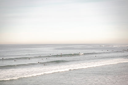 A wide landscape surf wall decor shot of Pacific Beach, showing many surfers in the water catching gentle waves under a hazy sky. This neutral surf print is great for beach art. 