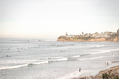 Landscape surf wall decor at Tourmaline Surf Park, Pacific Beach, San Diego, with numerous surfers in the water and a residential cliffside. 