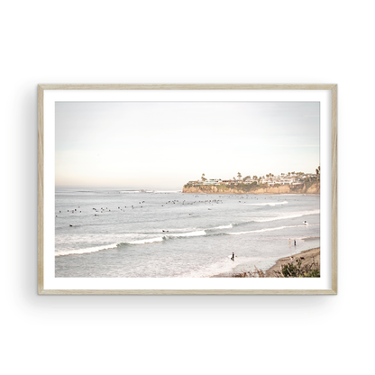Landscape surf wall decor at Tourmaline Surf Park, Pacific Beach, San Diego, with numerous surfers in the water and a residential cliffside. Photograph in minimalist mock up.