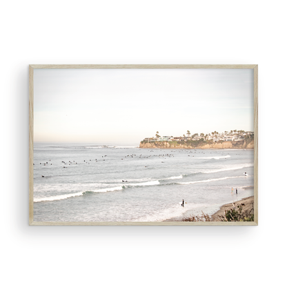 Landscape surf wall decor at Tourmaline Surf Park, Pacific Beach, San Diego, with numerous surfers in the water and a residential cliffside. Photograph in minimalist mock up.
