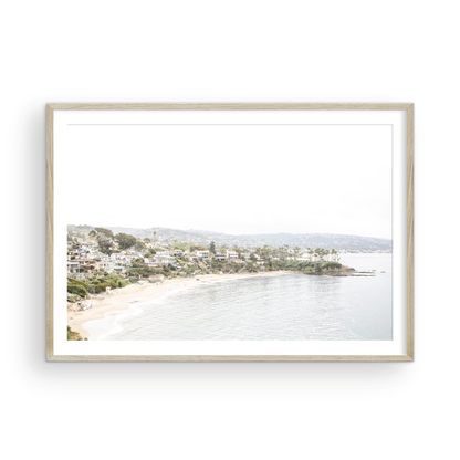 Horizontal coastal photography featuring a beach scene with a calm ocean and beach homes lining the shoreline, located in Laguna California. Photograph in minimalist mock up.