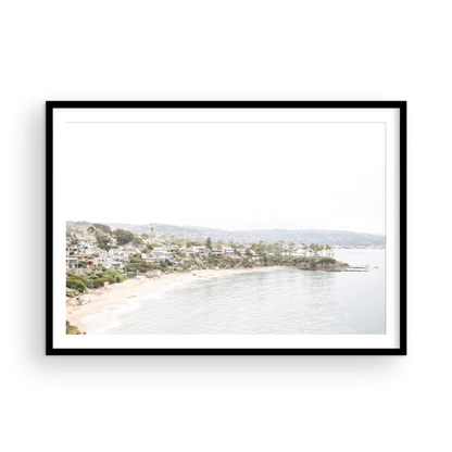Horizontal coastal photography featuring a beach scene with a calm ocean and beach homes lining the shoreline, located in Laguna California. Photograph in minimalist mock up.